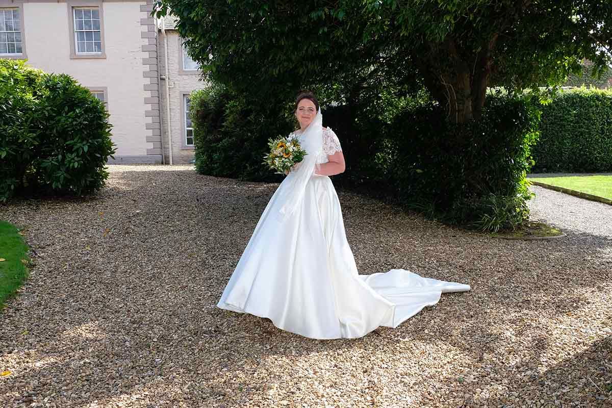 Bride in elegant white ball gown  holding bouquet on the gravel path outside Blaithwaite House Wigton's premier wedding venue