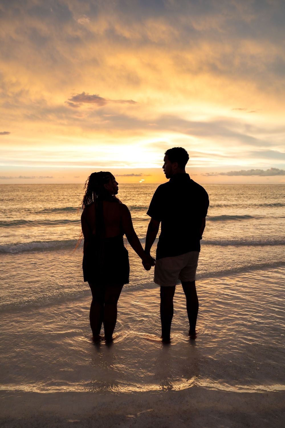 Romantic silhouette of a couple holding hands on the beach, watching a vibrant golden sunset over the ocean.