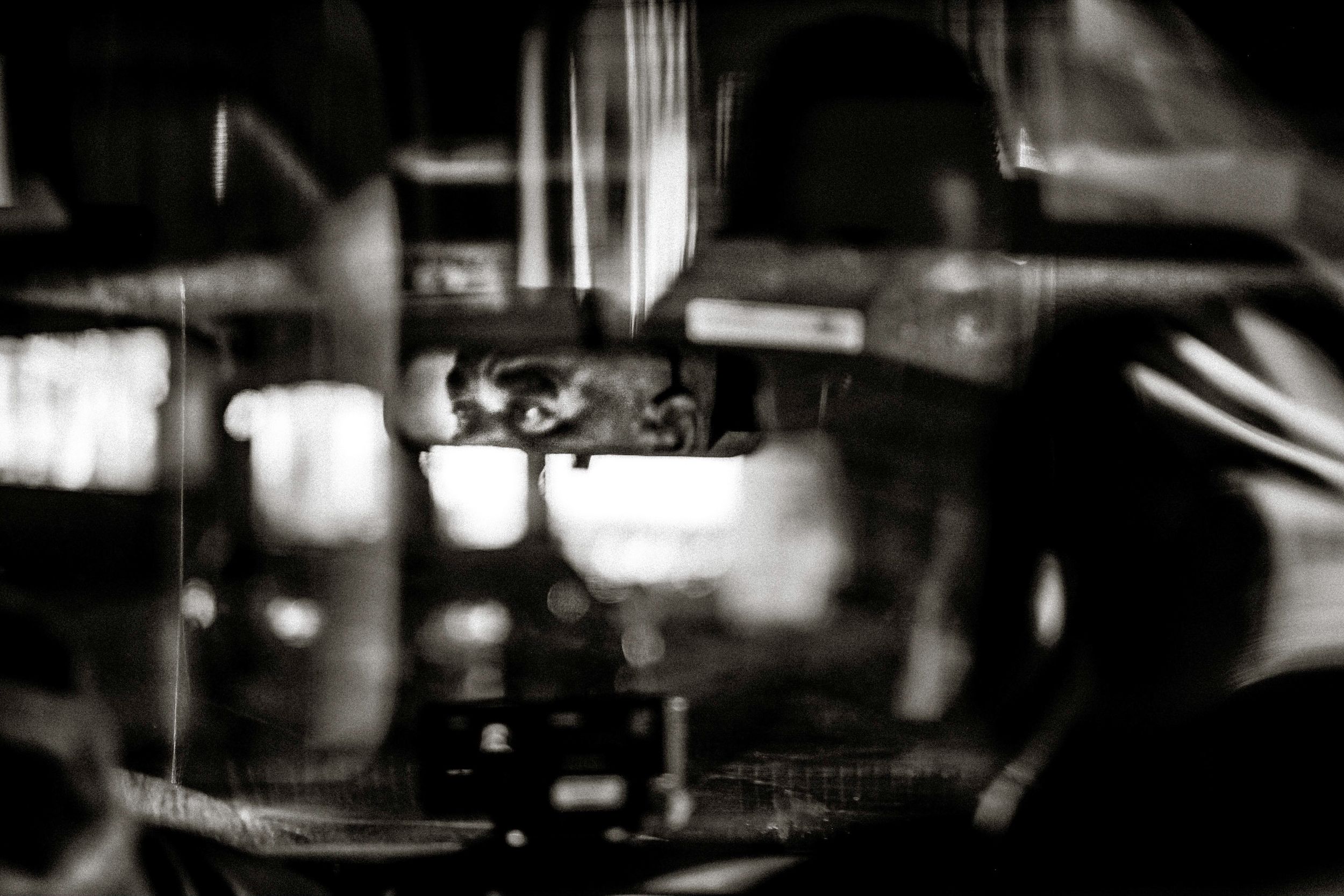 Black and white blurred photo of an espresso machine brewing coffee in a dimly lit cafe.