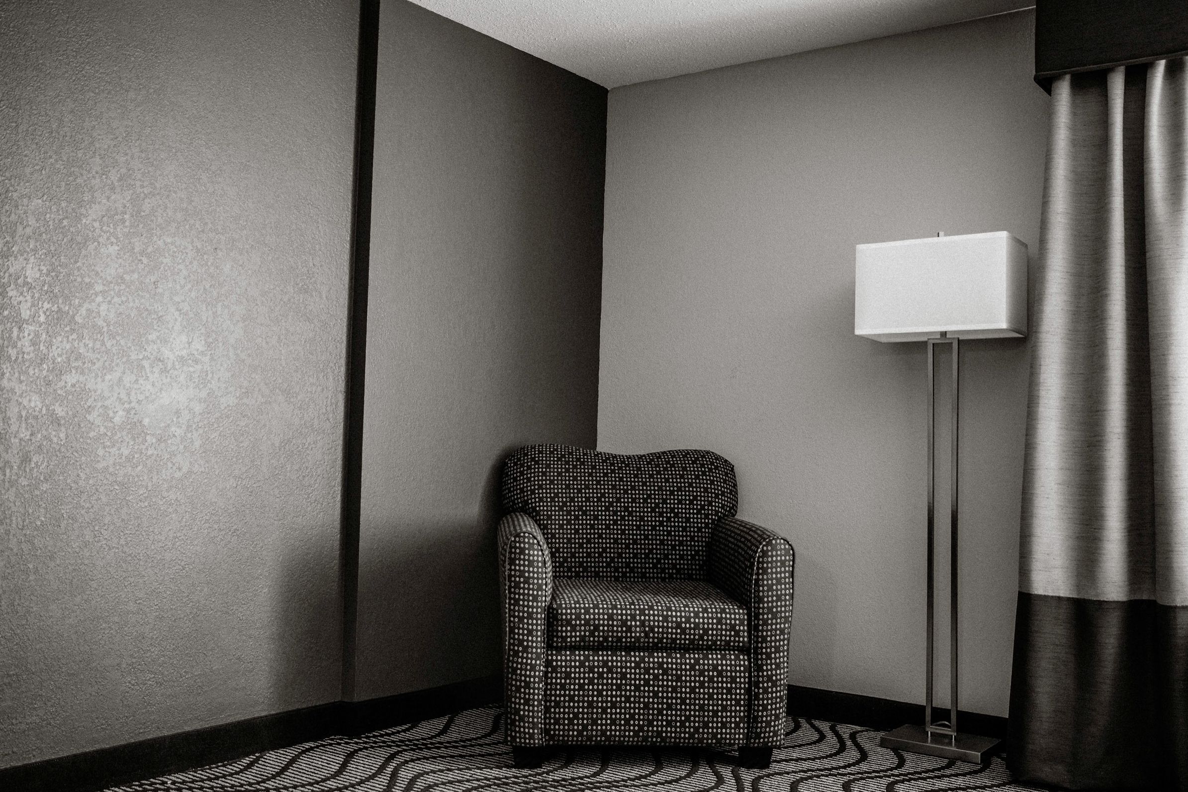 Elegant hotel room corner with a patterned armchair, floor lamp, and gray walls on a geometric carpet.