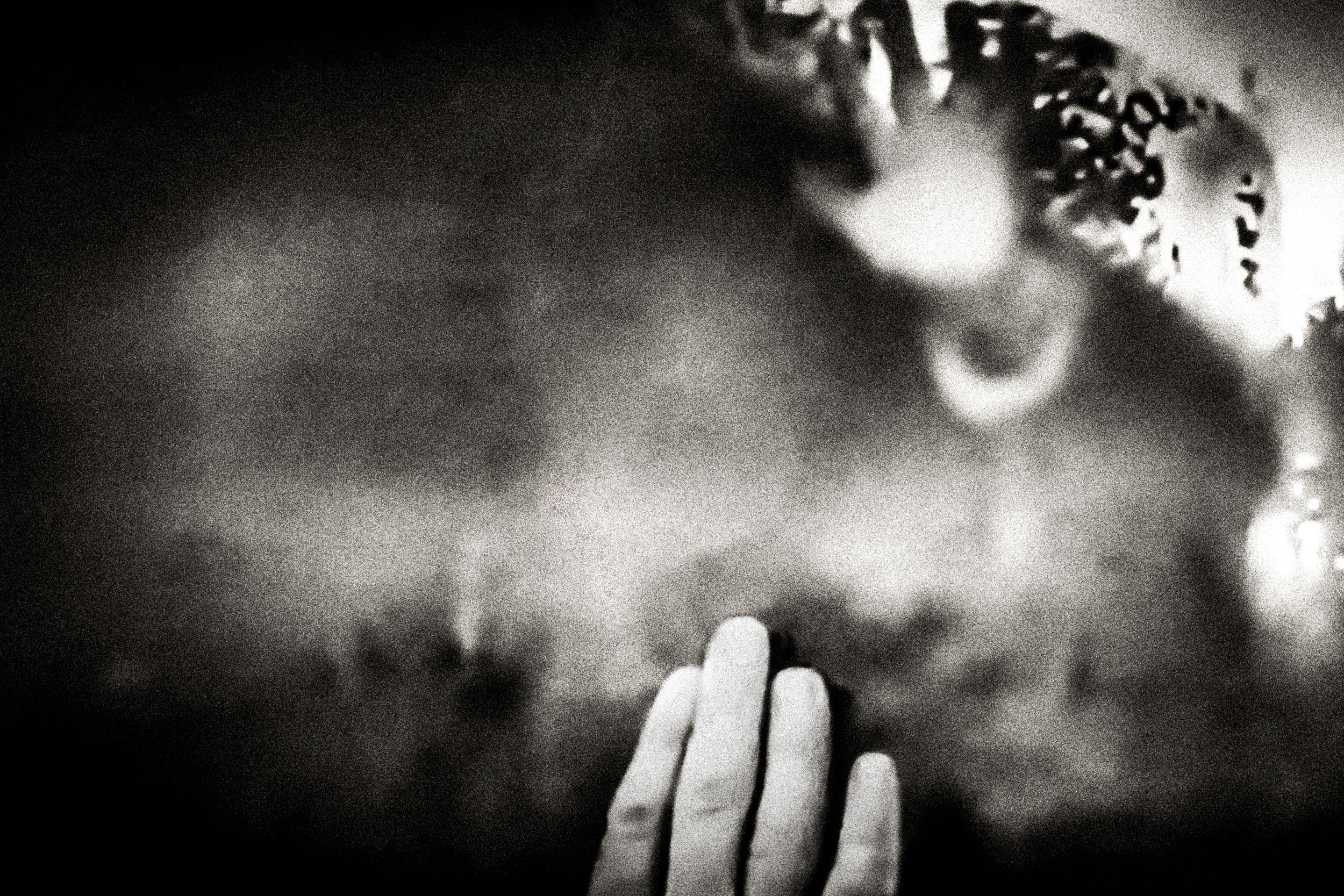Black and white photo of hands pressed together in prayer against a dark, moody background.
