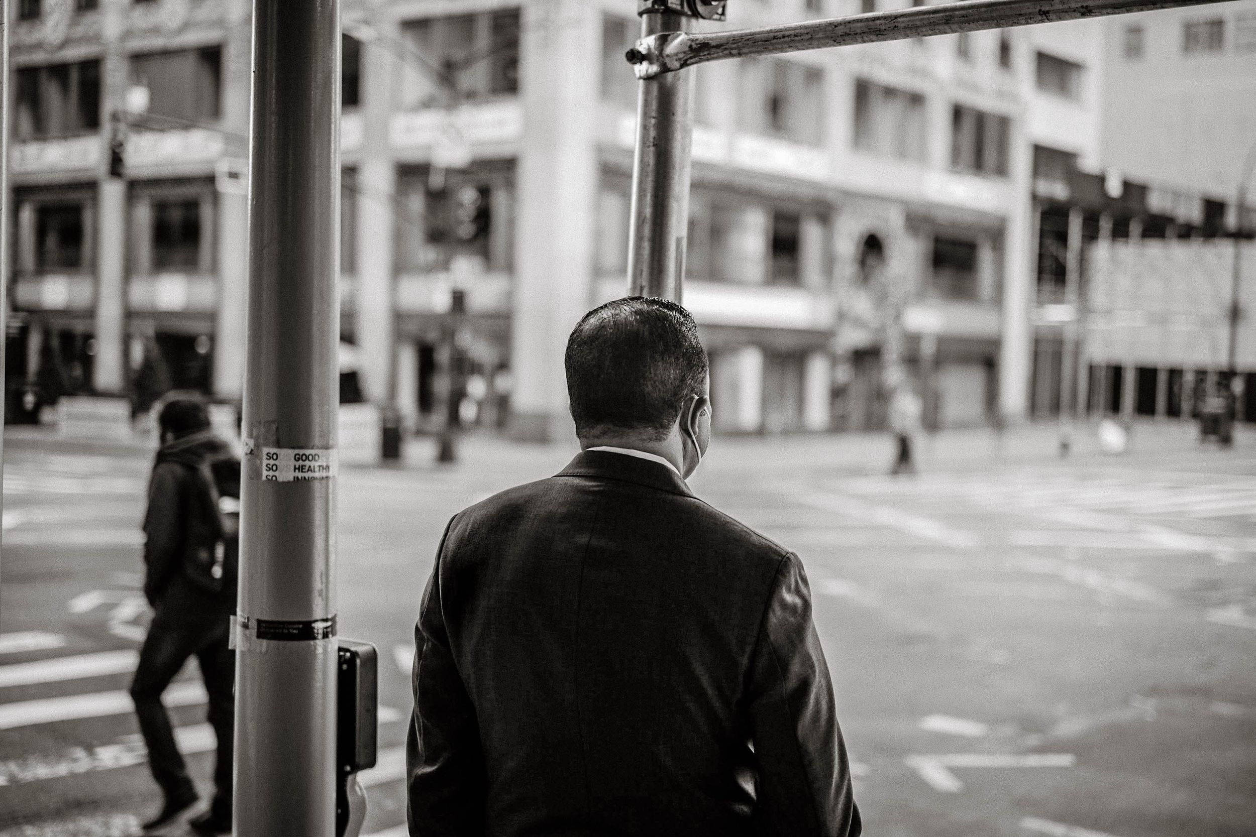 Man in leather jacket waiting at urban street corner in black and white.