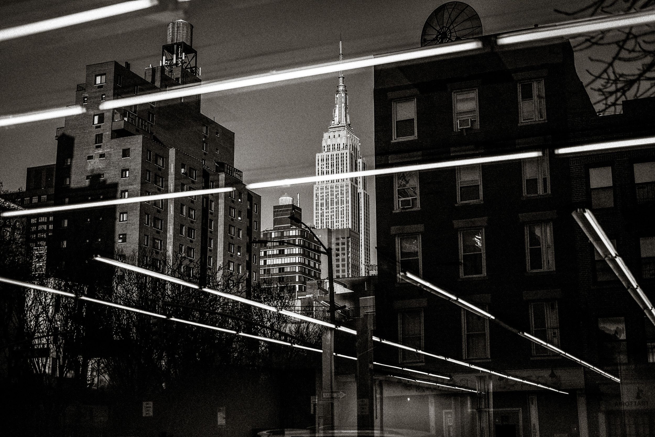 Black and white photo of NYC skyline with Empire State Building reflected in glass with neon light streaks.