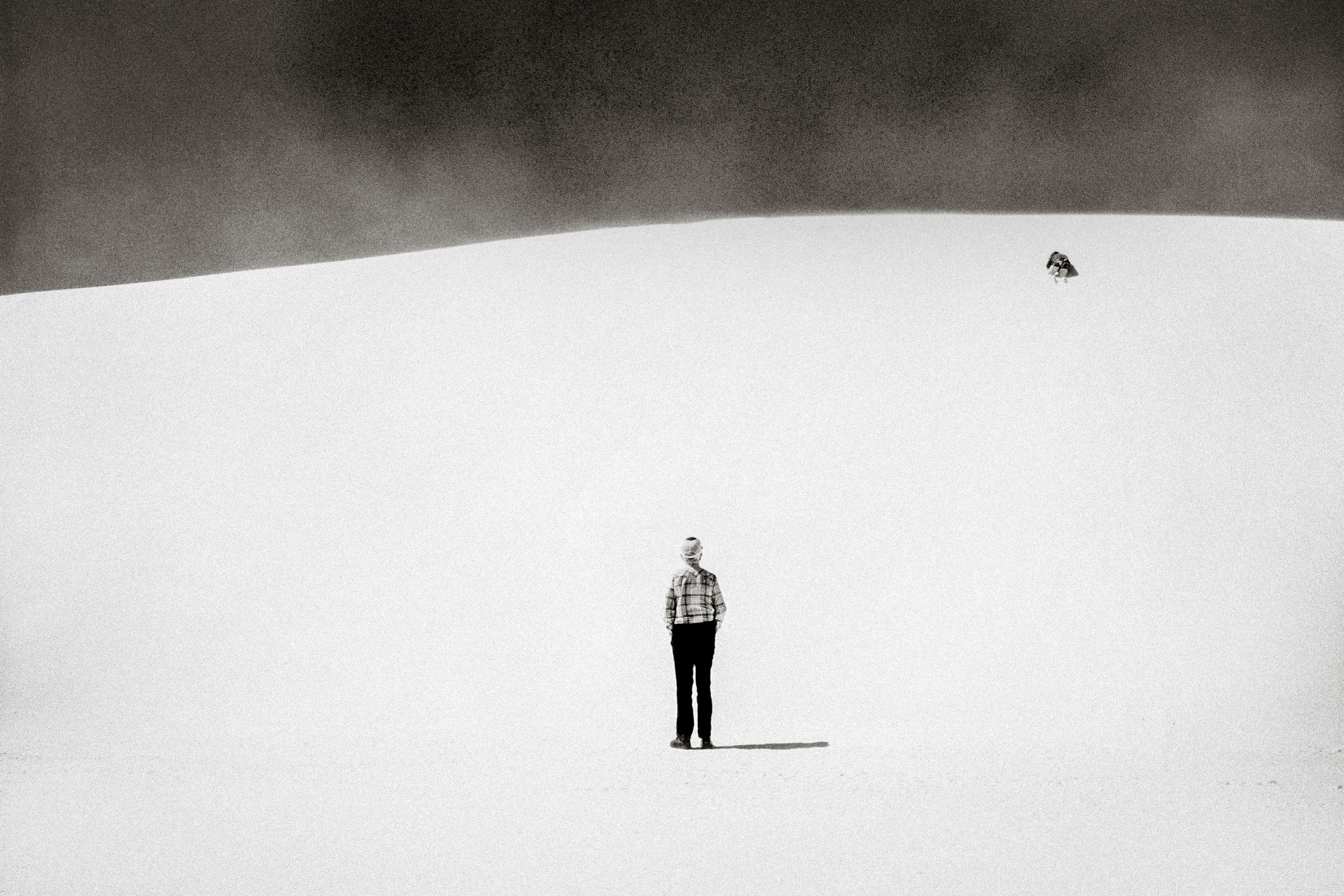 Black and white photo of a lone person standing on vast snowy dunes with a dark stormy sky.