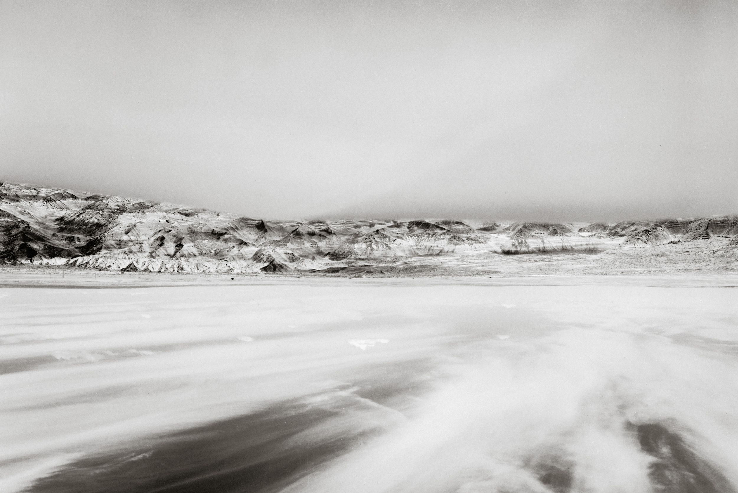 Black and white long exposure photo of ocean waves crashing on a beach with rocky cliffs in the misty background.