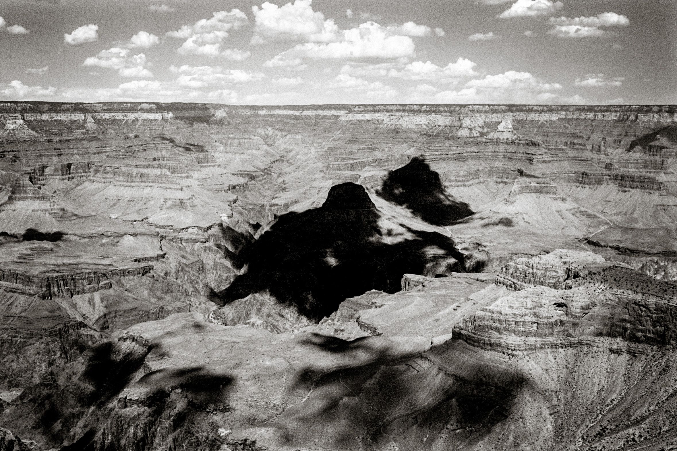 Black and white aerial view of the Grand Canyon showcasing dramatic rock formations and vast canyon depths under cloudy skies.