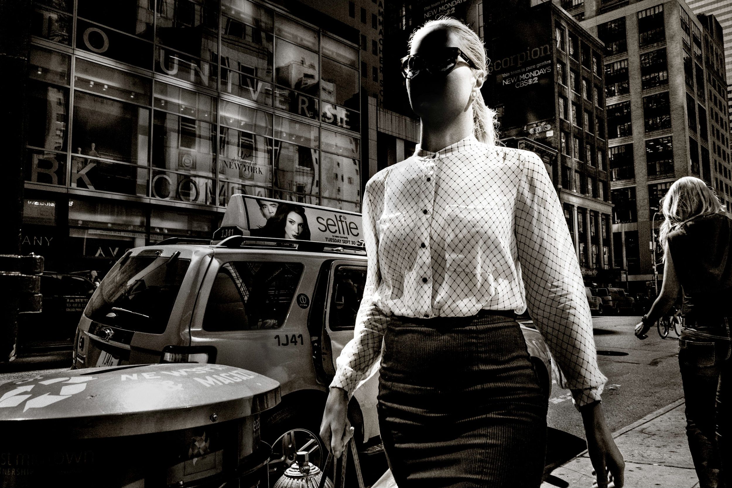 Black and white street photo of a woman in white blouse and skirt walking confidently in a busy city.