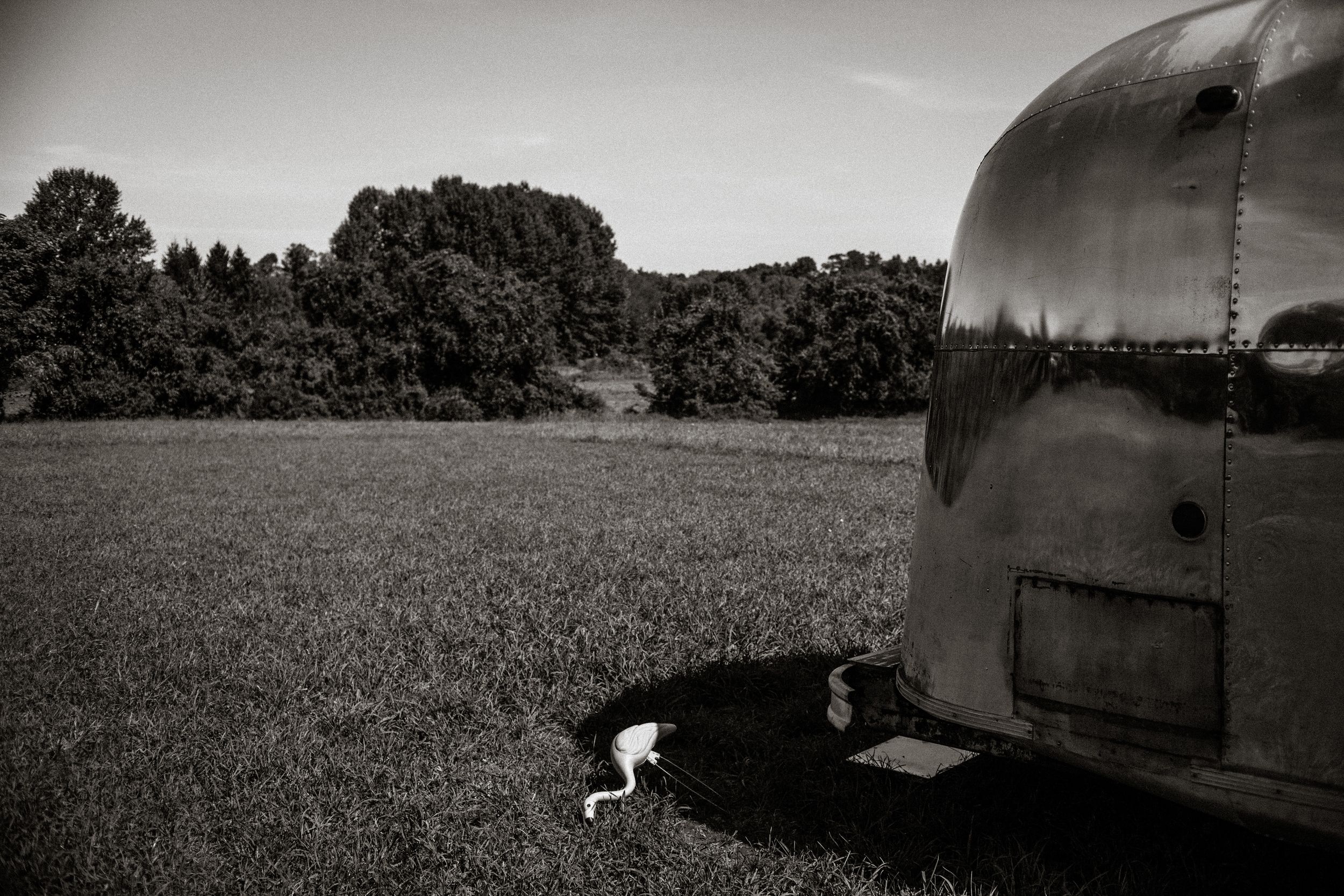 Black and white photo of a vintage Airstream trailer parked in a lush green field with trees in the background.