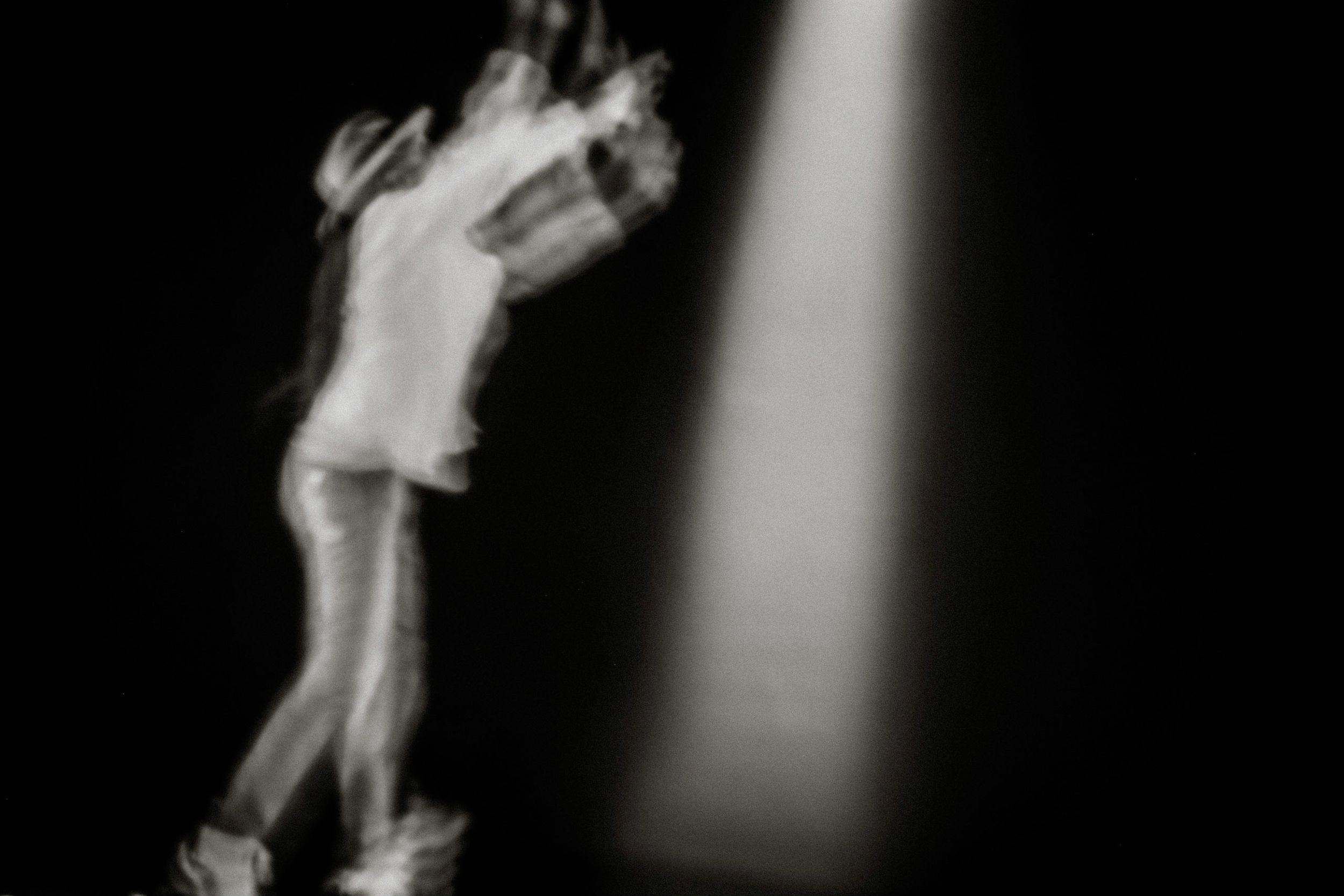 Blurred black and white photo of a dancer performing under a spotlight on a dark stage.