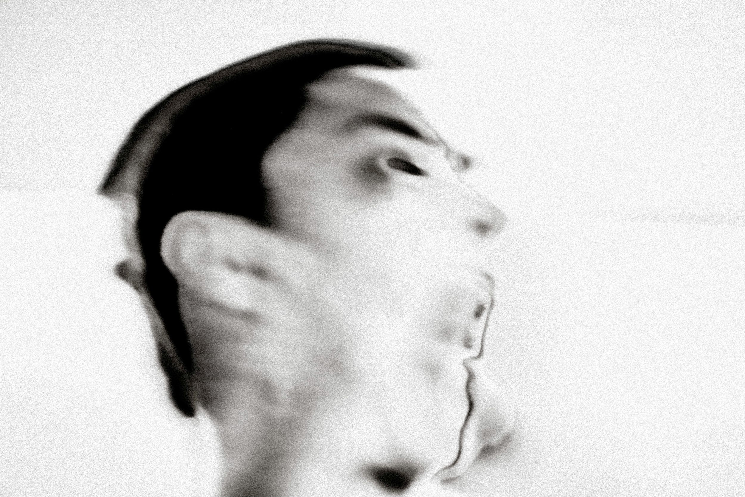 Blurred black and white portrait of a man's face with motion blur effect creating an abstract, ghostly appearance.