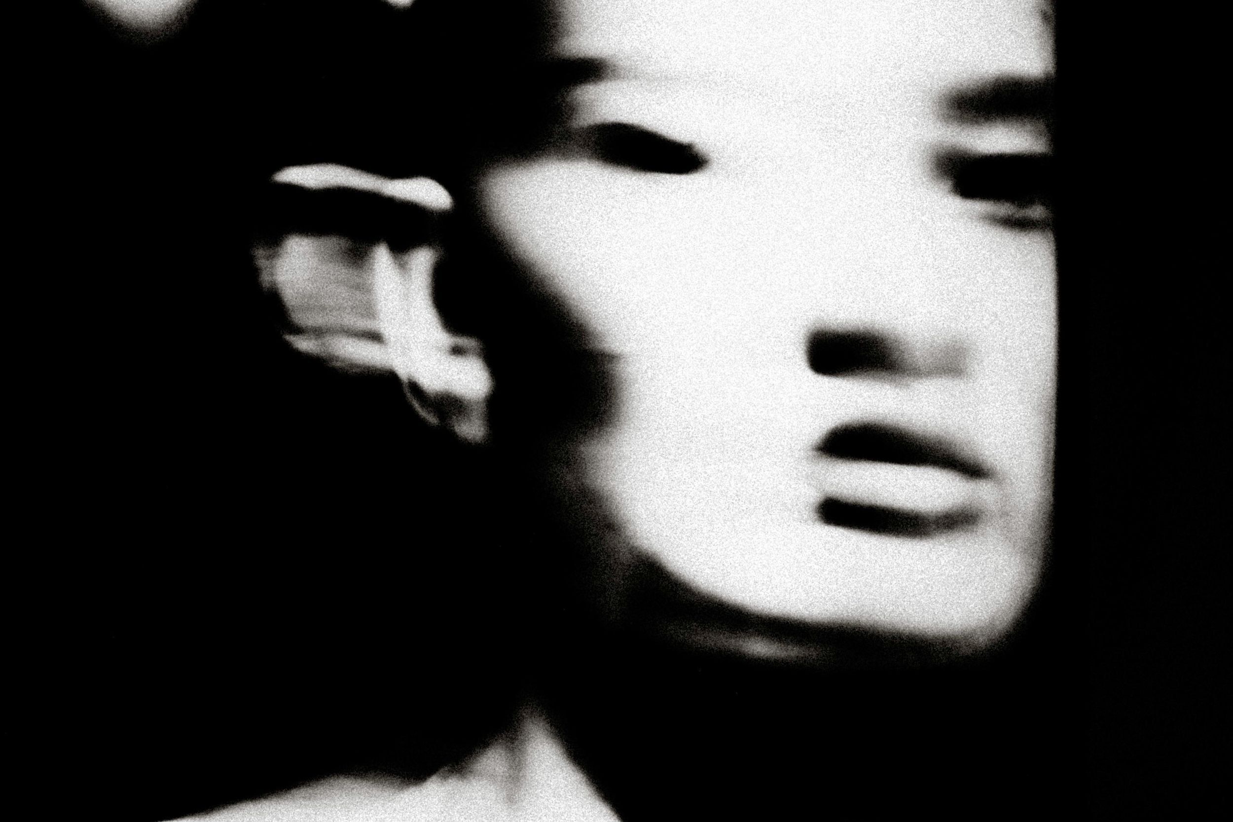 Blurred black and white portrait of a person with motion blur effect creating an ethereal, ghostly appearance.