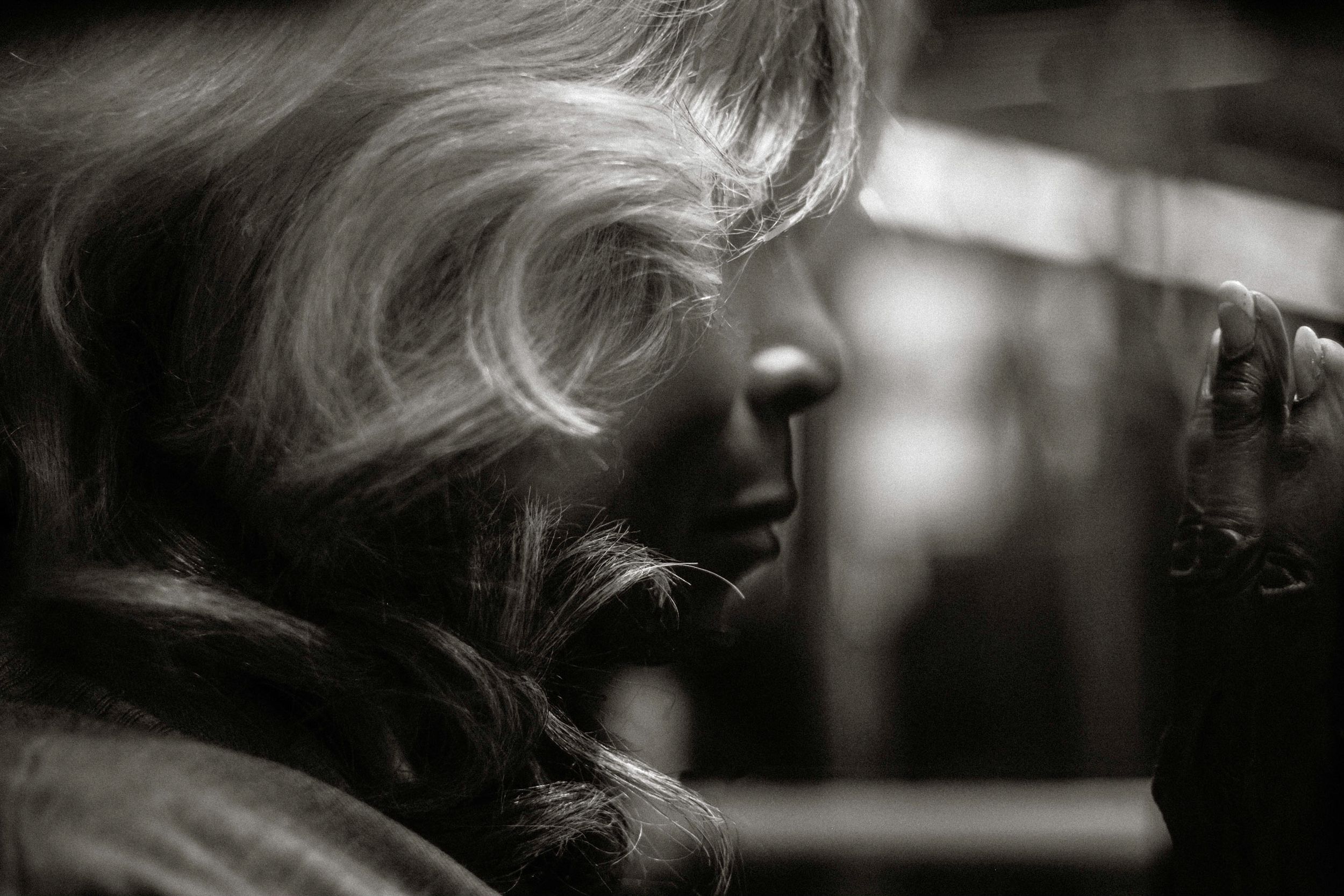 Black and white portrait of a blonde woman in profile, hand raised to her face, with dramatic lighting.