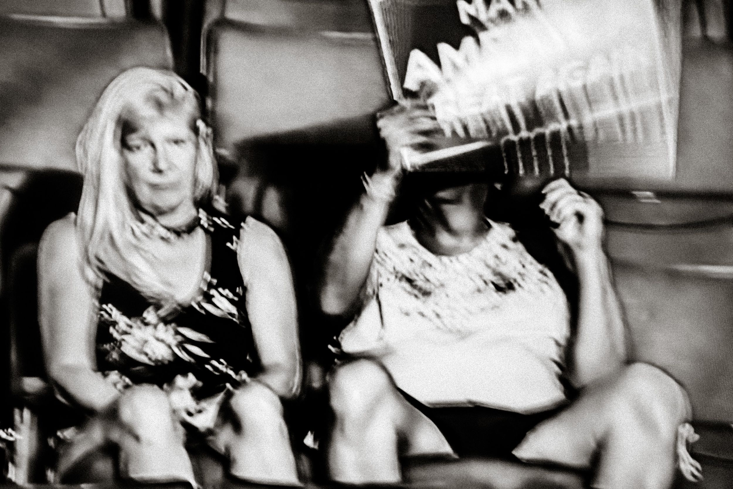 Black and white photo of two women sitting at an event, one holding a sign above her head.