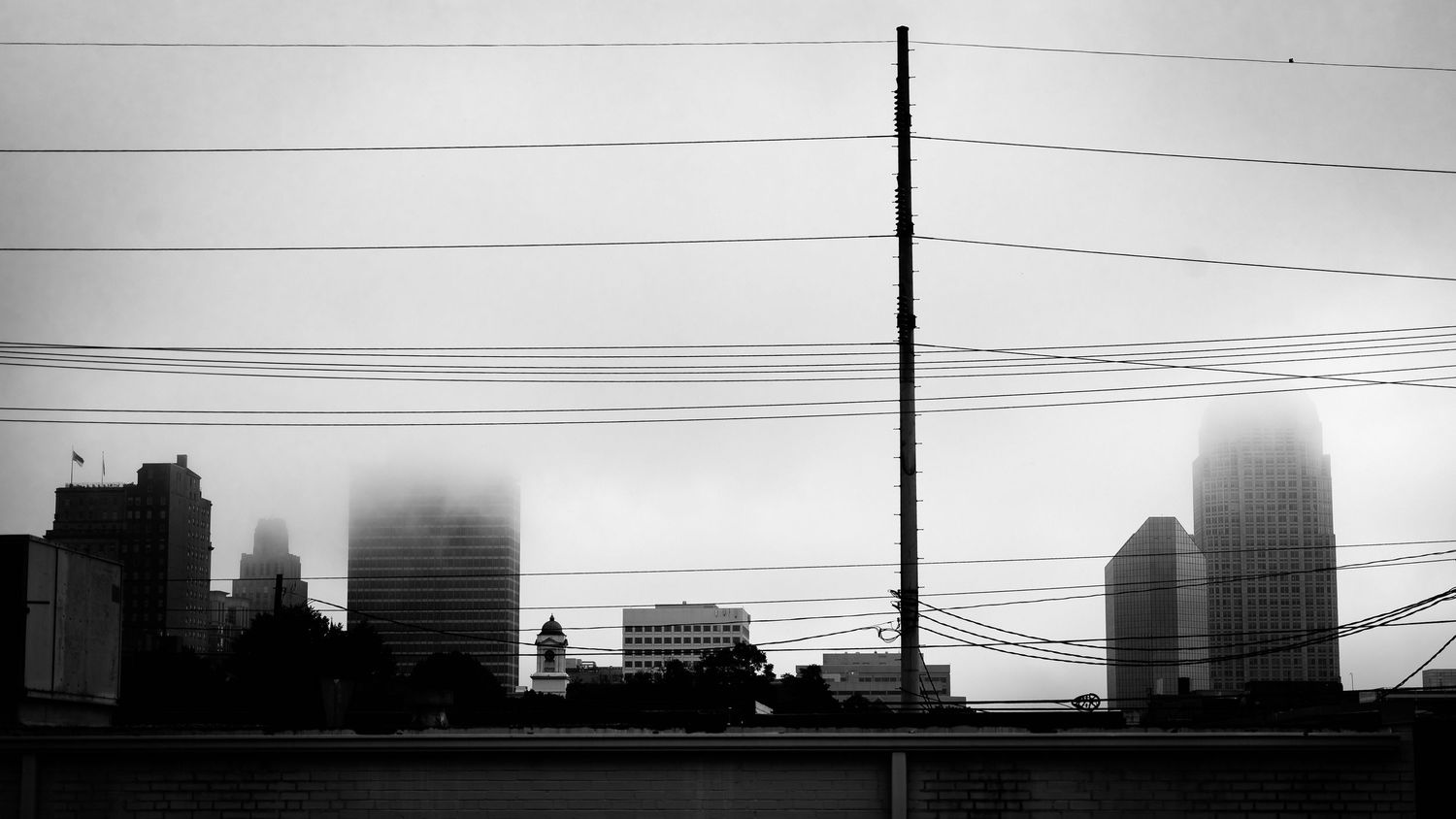Foggy black and white cityscape with skyscrapers partially obscured by mist, power lines, and a tall utility pole.