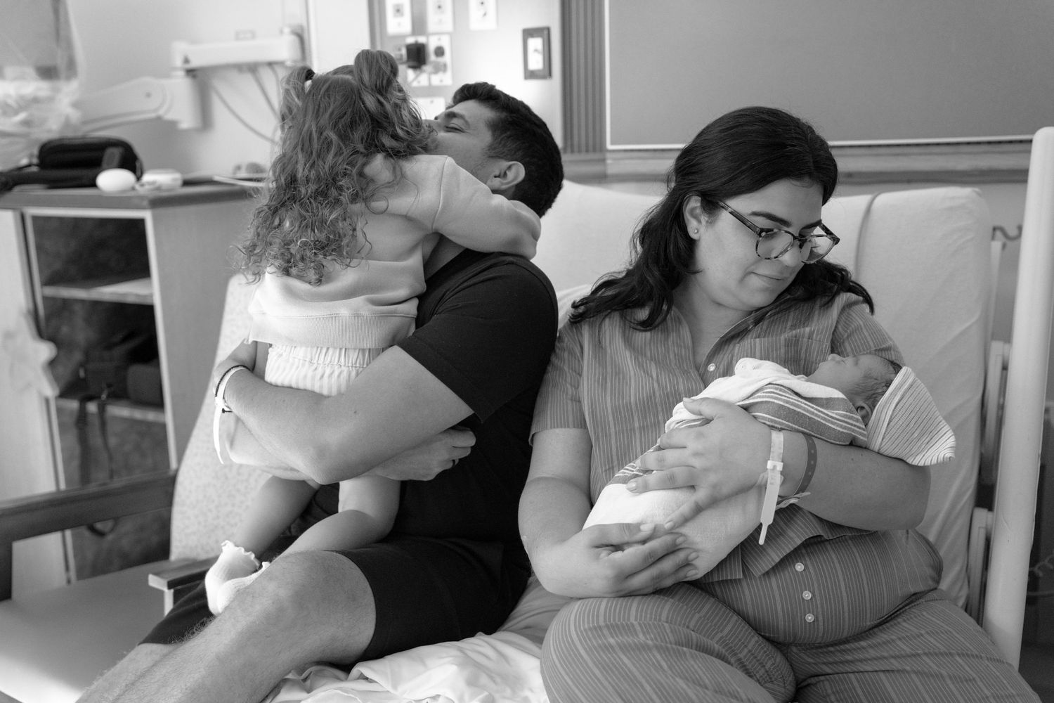 Black and white hospital photo of parents with newborn baby and toddler, a tender family moment after birth.