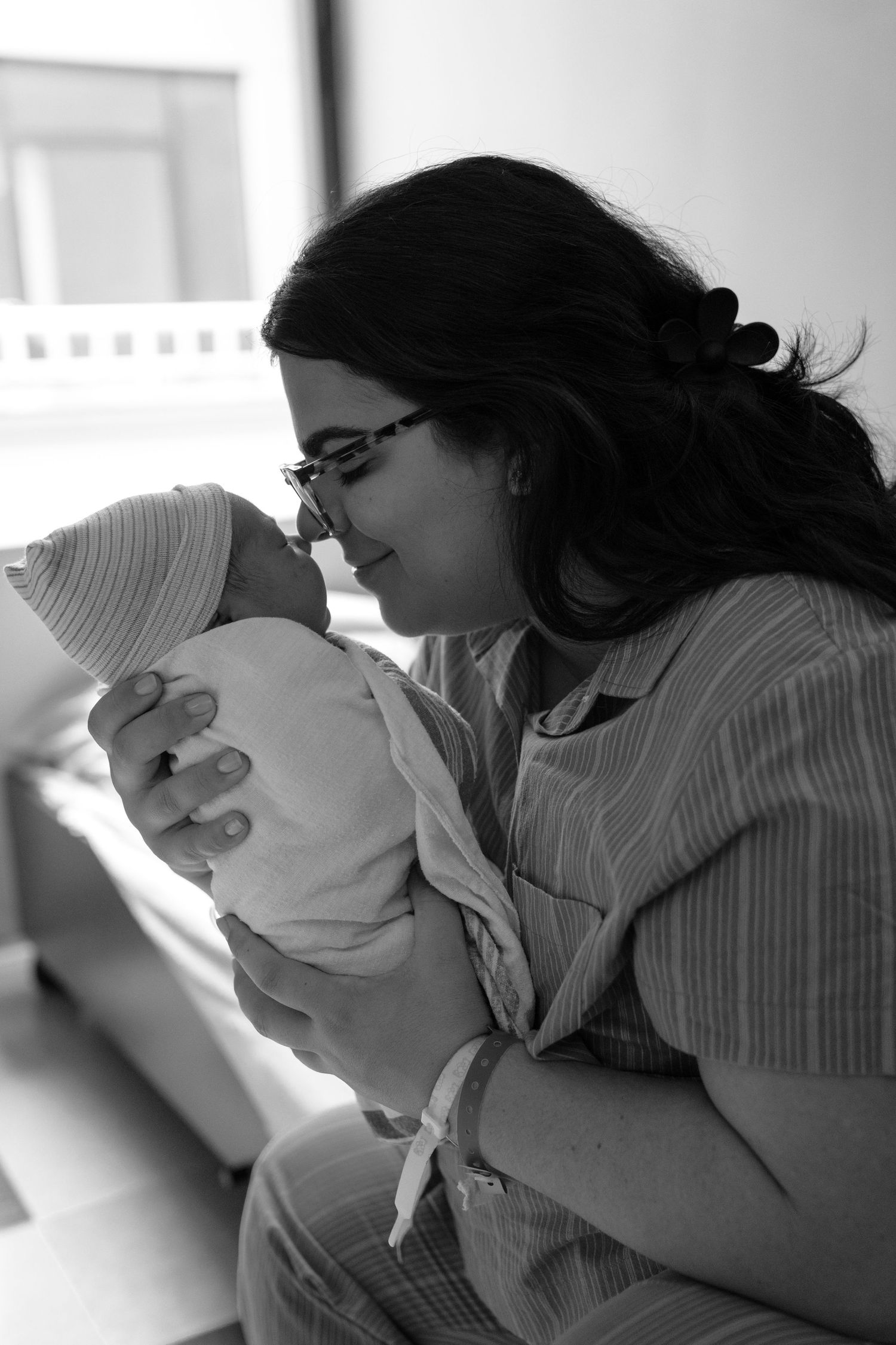 Black and white photo of a new mother in hospital gown holding and gazing lovingly at her newborn baby.