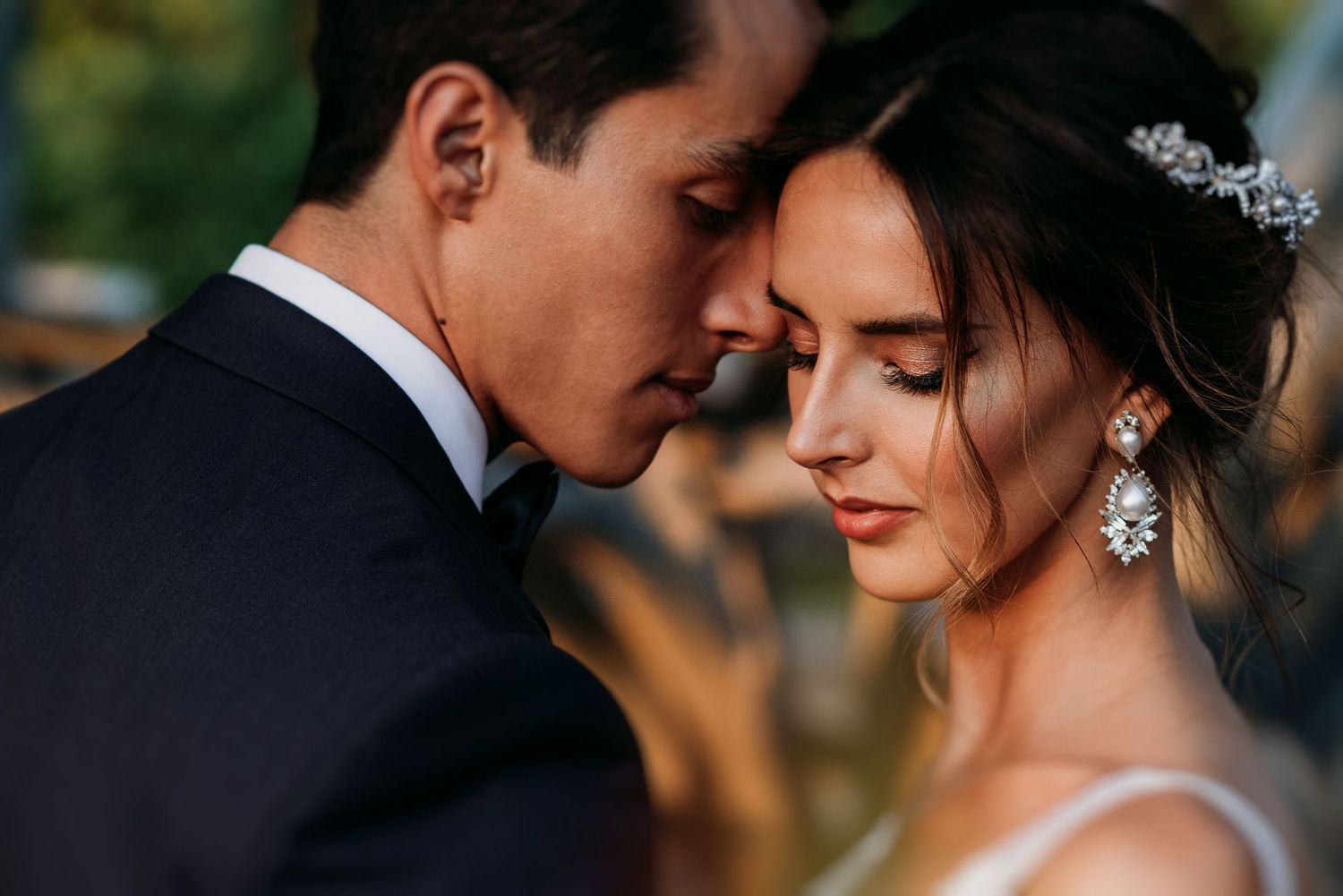 Bride and groom share an intimate forehead touch moment, bride wearing crystal earrings and hair piece on wedding day.