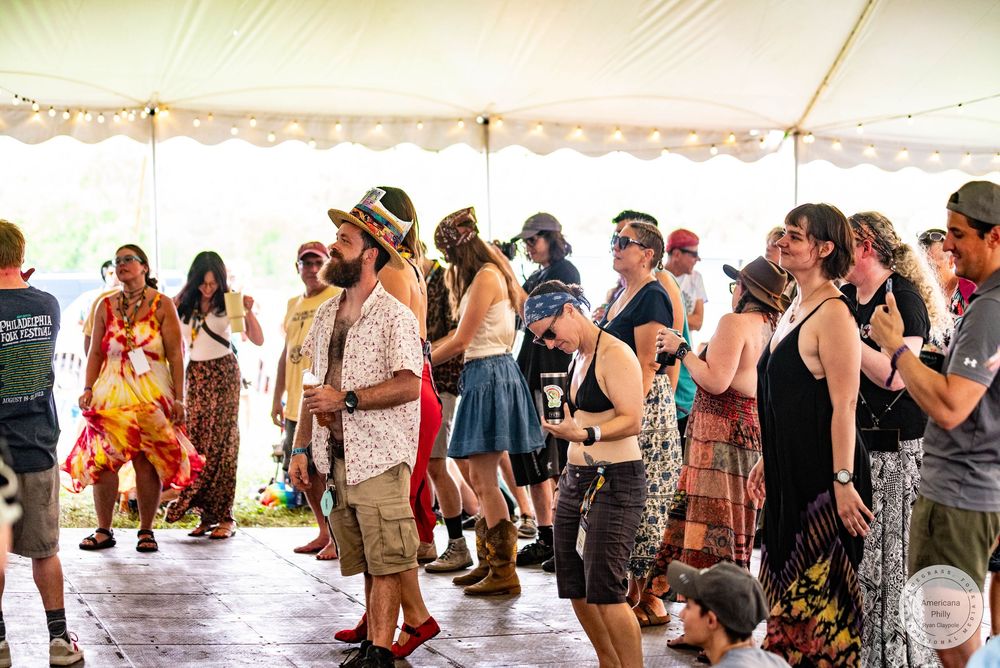 Festival crowd dancing under a white tent at an outdoor music event on a sunny day.
