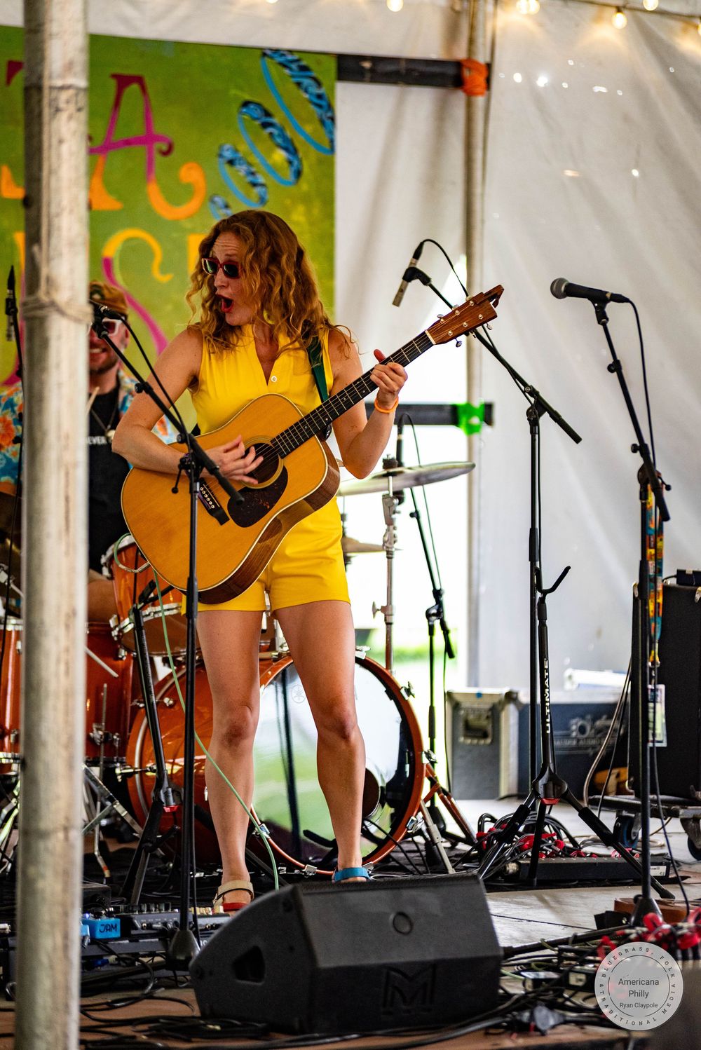 Woman in yellow dress playing acoustic guitar on stage at outdoor music festival.