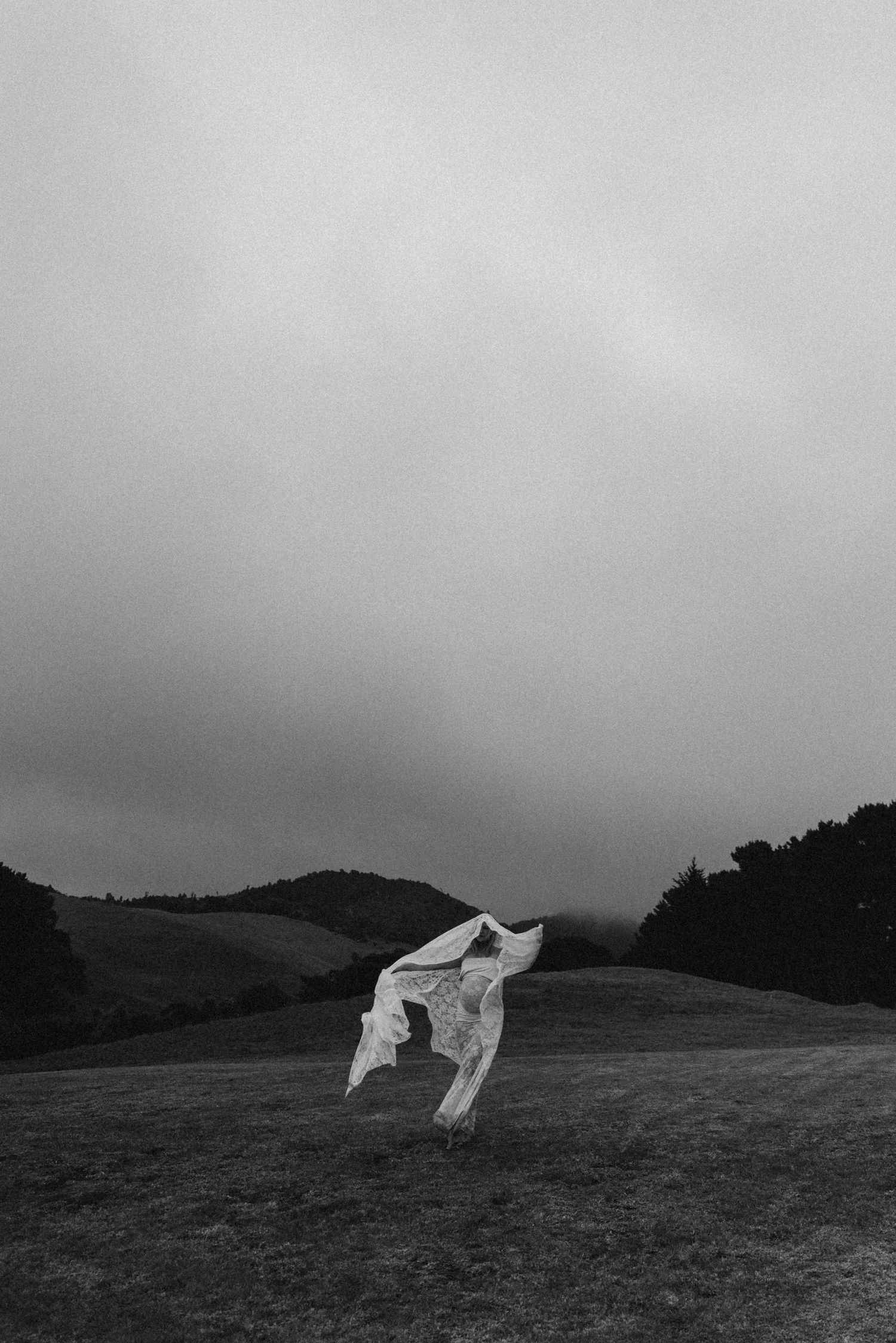 Black and white photo of white fabric blowing in wind on a misty hilltop landscape.