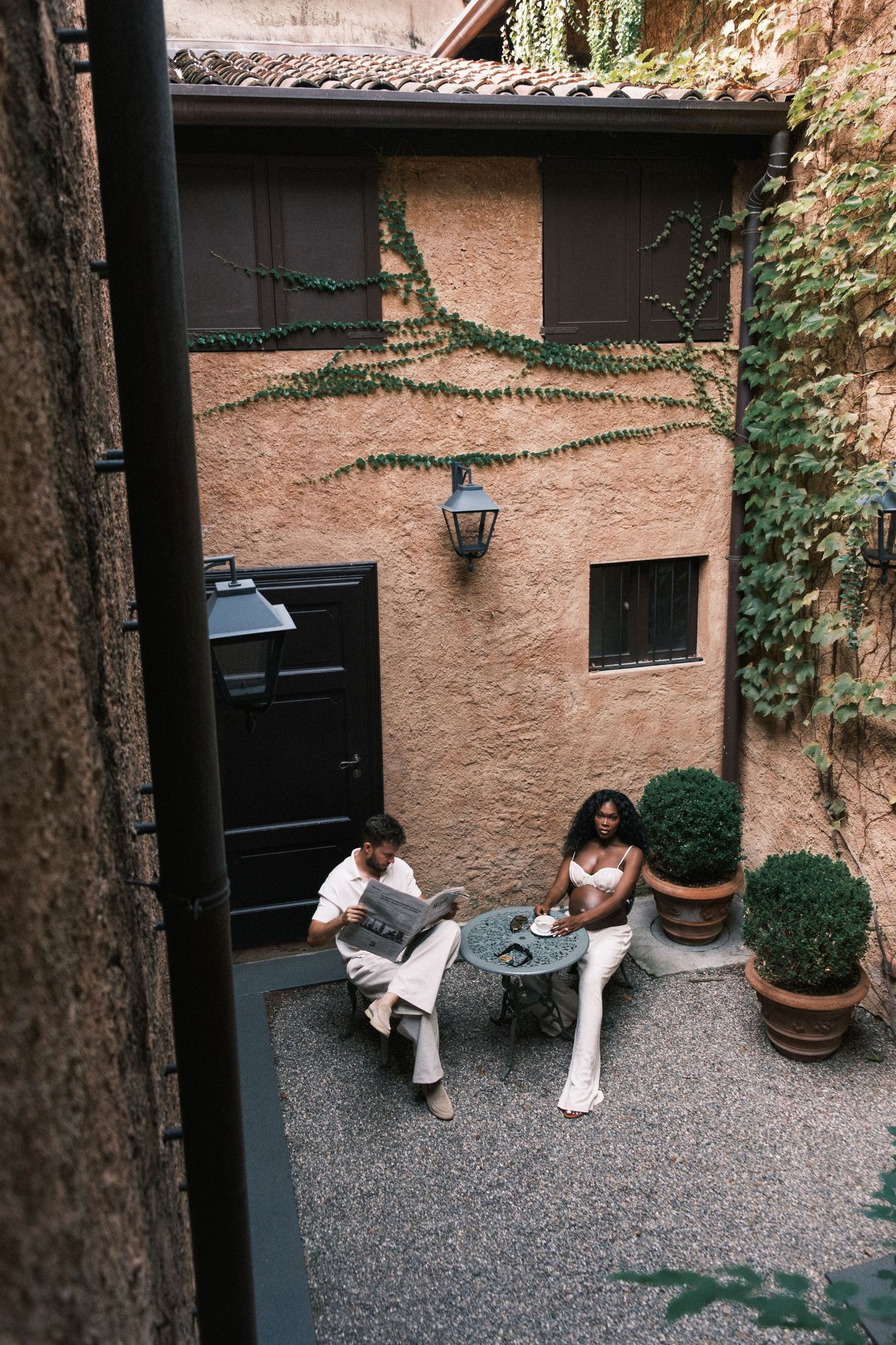 Couple relaxing in a charming Mediterranean courtyard with ivy-covered walls, potted plants, and a small bistro table.