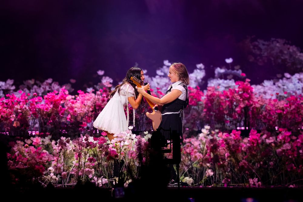 Olivia Rodrigo singing alongside her guitarist on a flower-covered stage during opening night of the Unraveled Tour at PeoplesBank Arena
