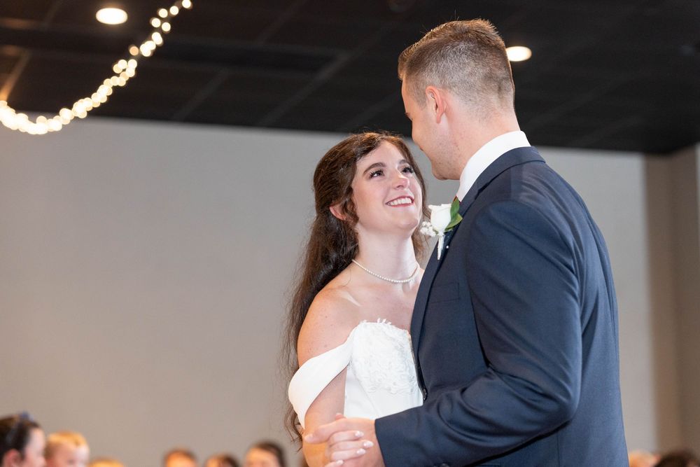 Bride and groom share their first dance, smiling at each other in elegant wedding attire at a decorated reception venue.