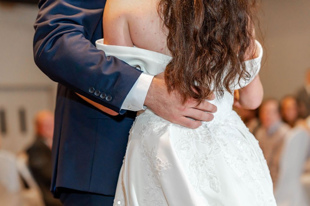 Bride and groom sharing their first dance, groom in navy suit embracing bride in white lace wedding gown.