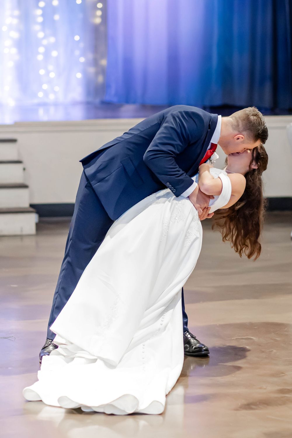 Bride and groom sharing a romantic dip kiss during their first dance at a wedding reception.