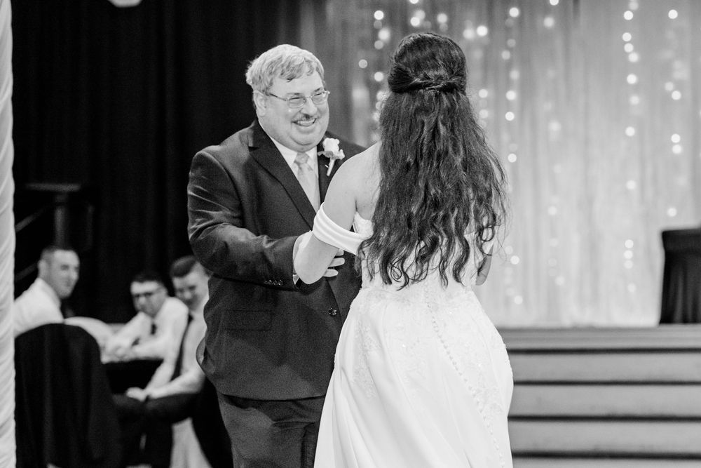 Father-daughter wedding dance in black and white, sharing a joyful moment on the dance floor.