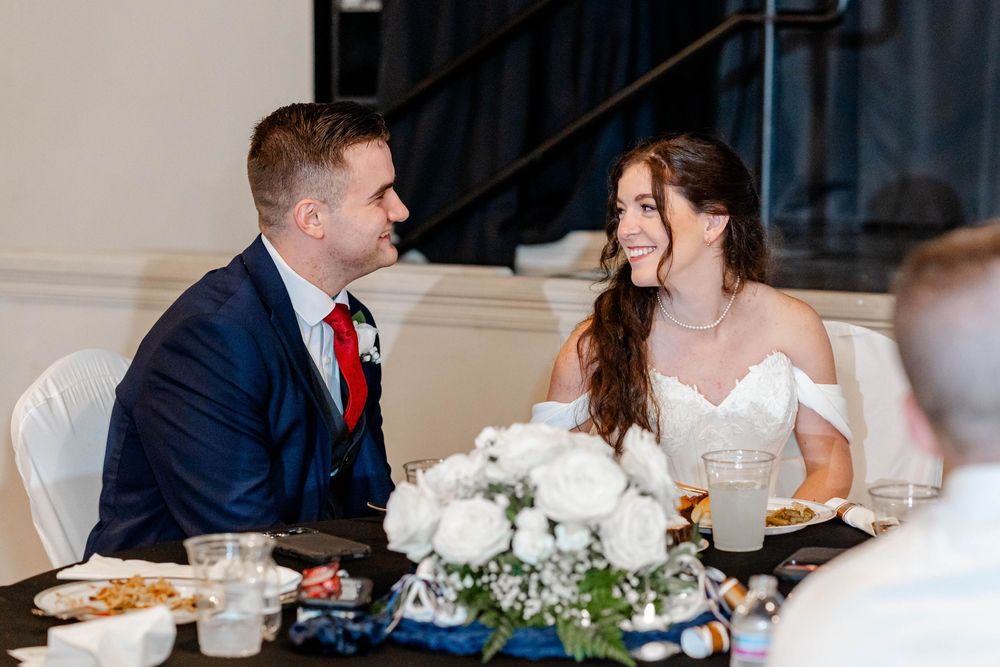 Bride and groom share a joyful moment at their wedding reception table adorned with white floral centerpieces.