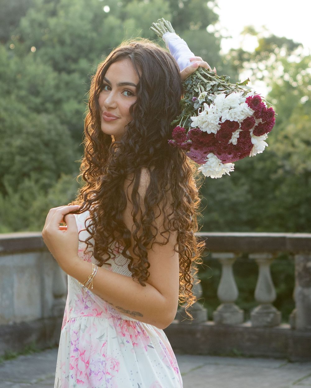 Woman in floral dress holding a bouquet of red and white flowers in a garden setting.