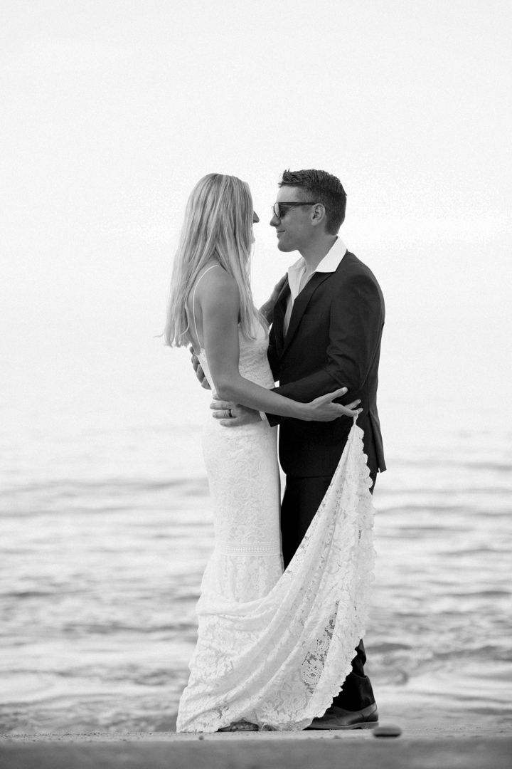 Black and white photo of a couple in wedding attire embracing by the ocean, sharing a romantic moment.