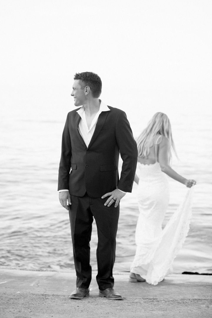 Black and white photo of a groom in a suit and bride in a white dress standing by the ocean shore.