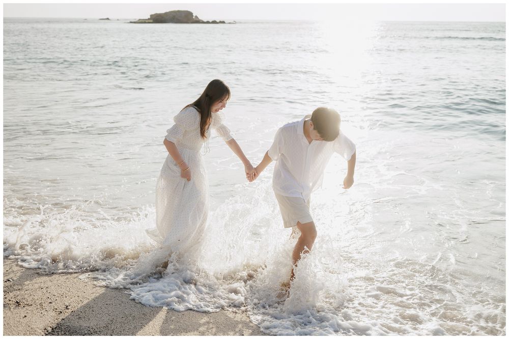 St. Regis Punta Mita Photographer documenting a couple walking hand in hand through the ocean waves on a sunny beach.