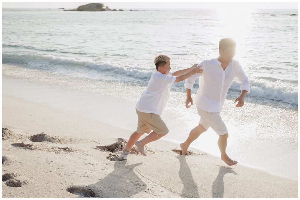 Punta Mita Family Photographer capturing a father and son running and playing together along the sunny beach by the ocean waves.