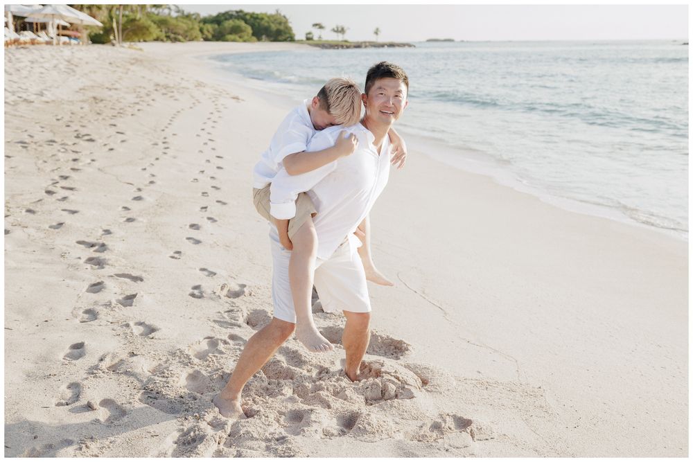 Family Photo Session capturing a father giving his son a playful piggyback ride on a sunny tropical beach.