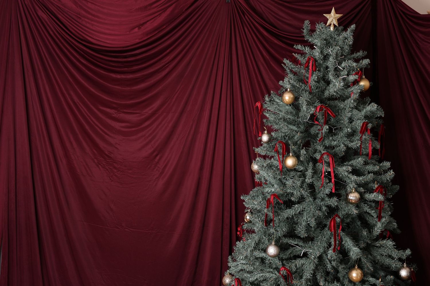 Elegant Christmas scene with decorated tree, wrapped gifts, white tufted bench, and rich burgundy draped curtains.