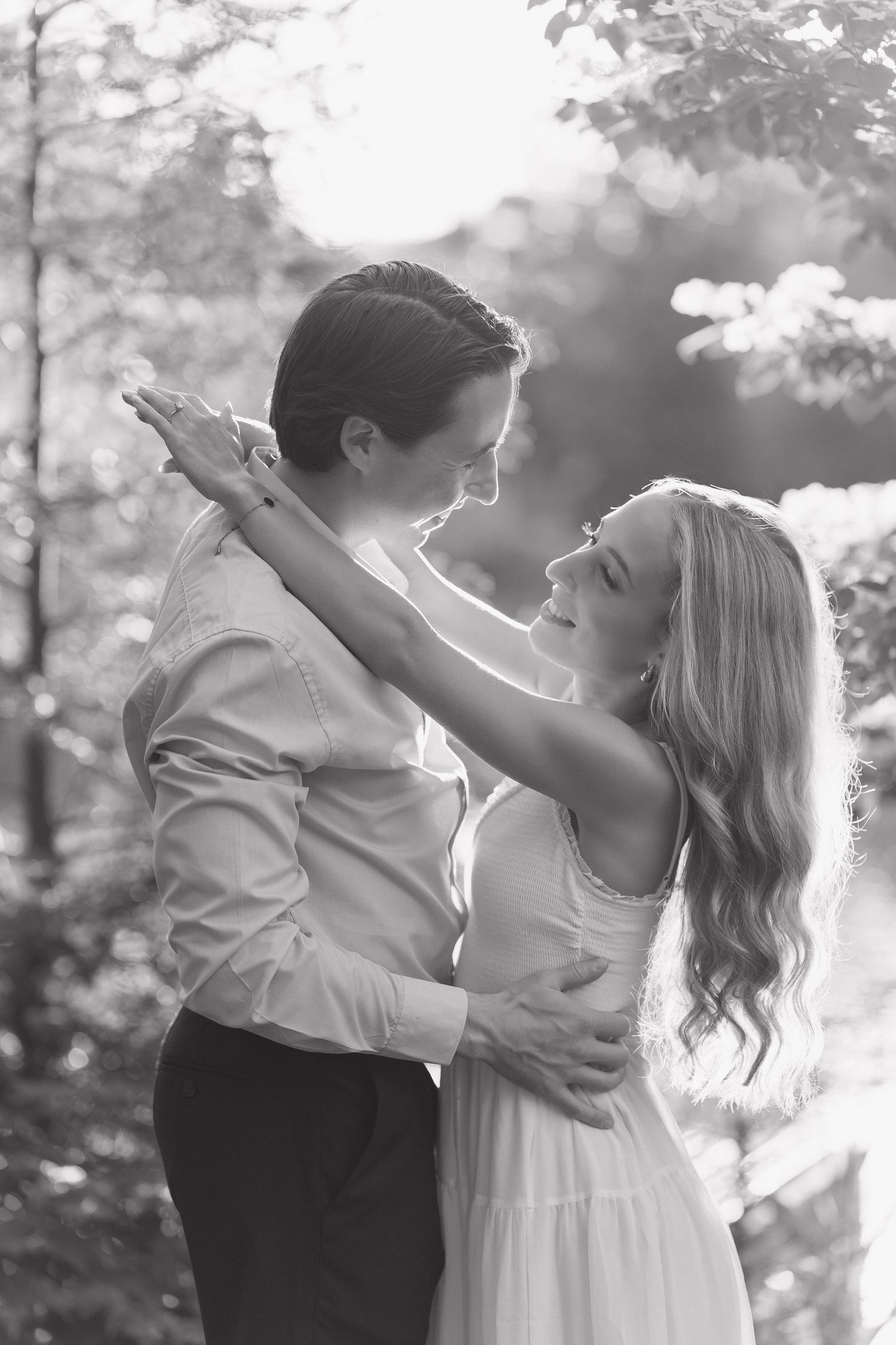 Black and white romantic portrait of couple embracing and gazing at each other in sunlit trees at Public Gardens.