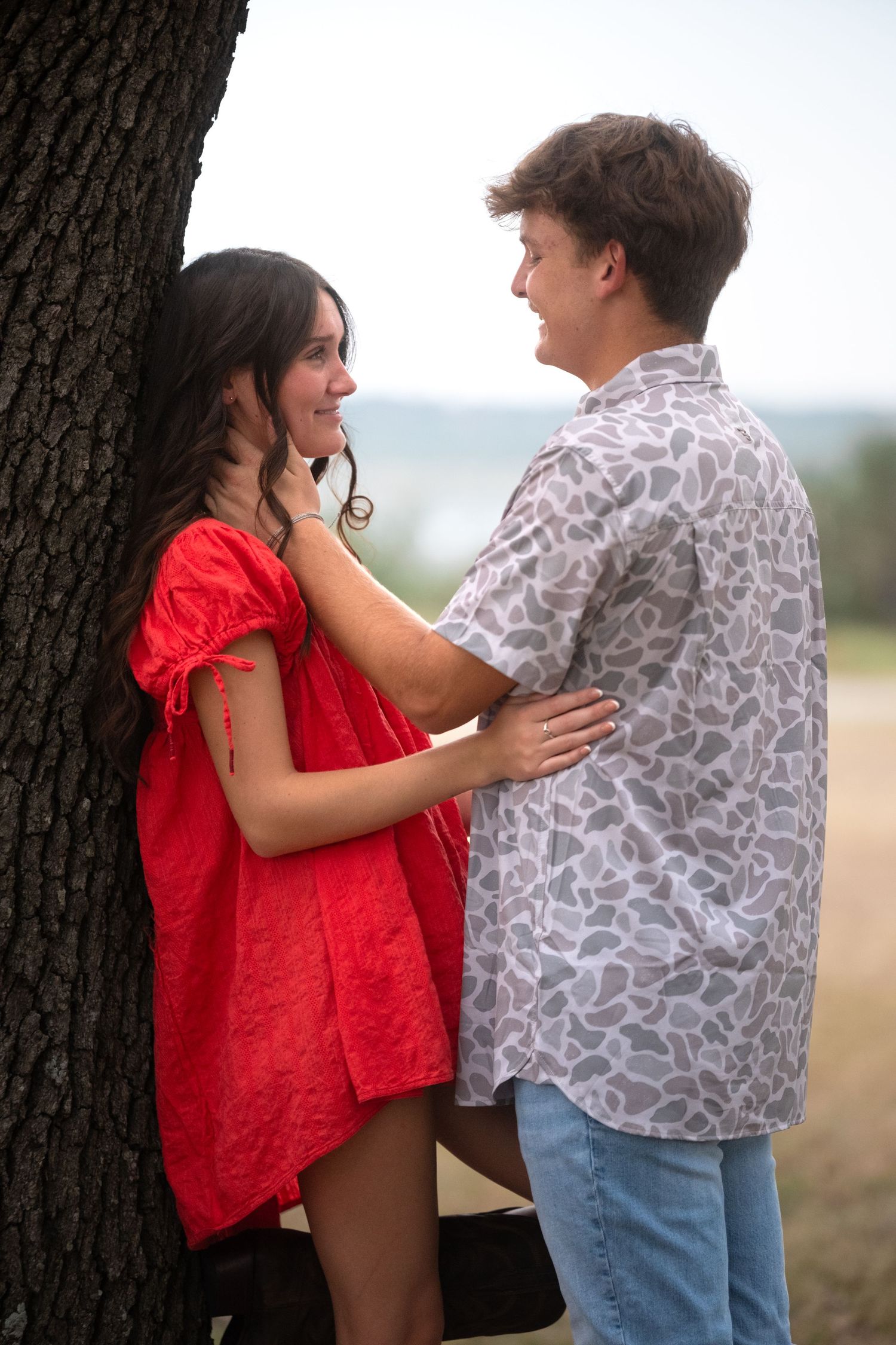 Young couple sharing a romantic moment leaning against a tree outdoors overlooking stillhouse hollow lake in Belton, Texas