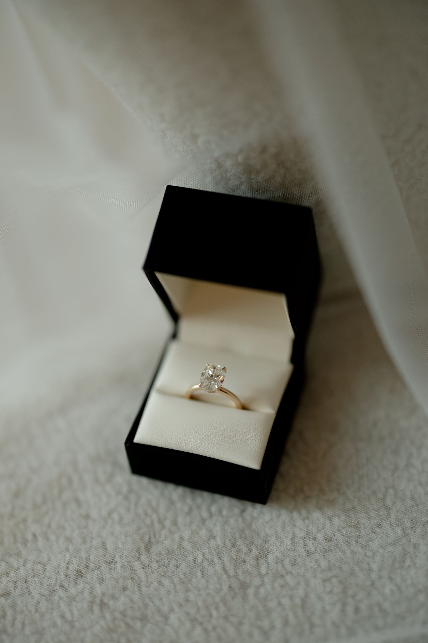 Close-up of diamond solitaire engagement ring displayed in black jewelry box on white fabric.