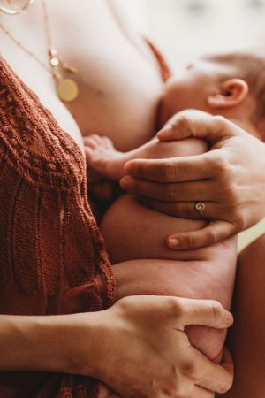 Close-up of supportive hands during intimate breastfeeding moment in warm lighting.