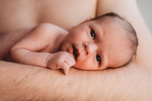 Close-up of an alert newborn baby with bright eyes lying on soft fabric.