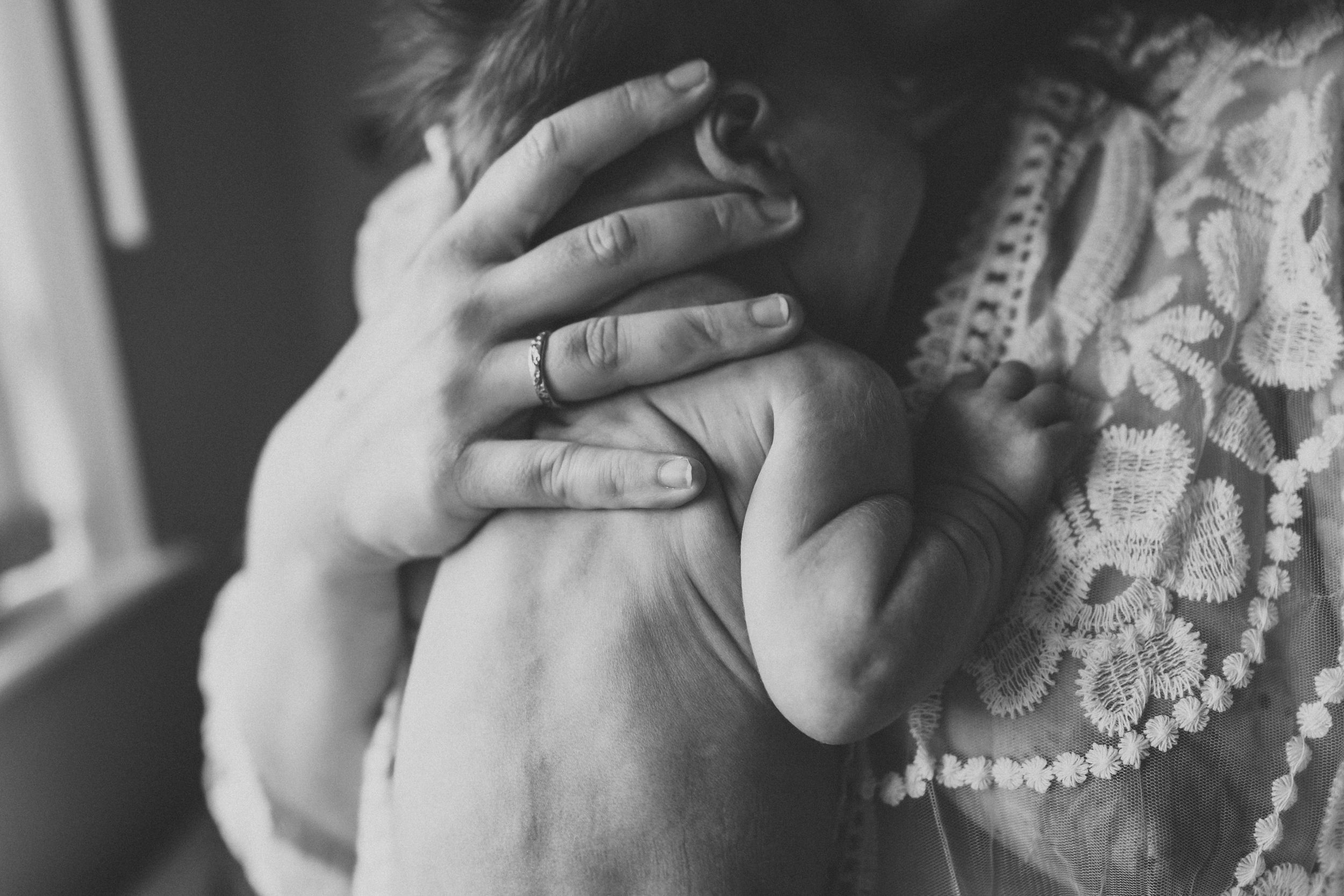 Black and white image of hands tenderly cradling a newborn wrapped in lace.