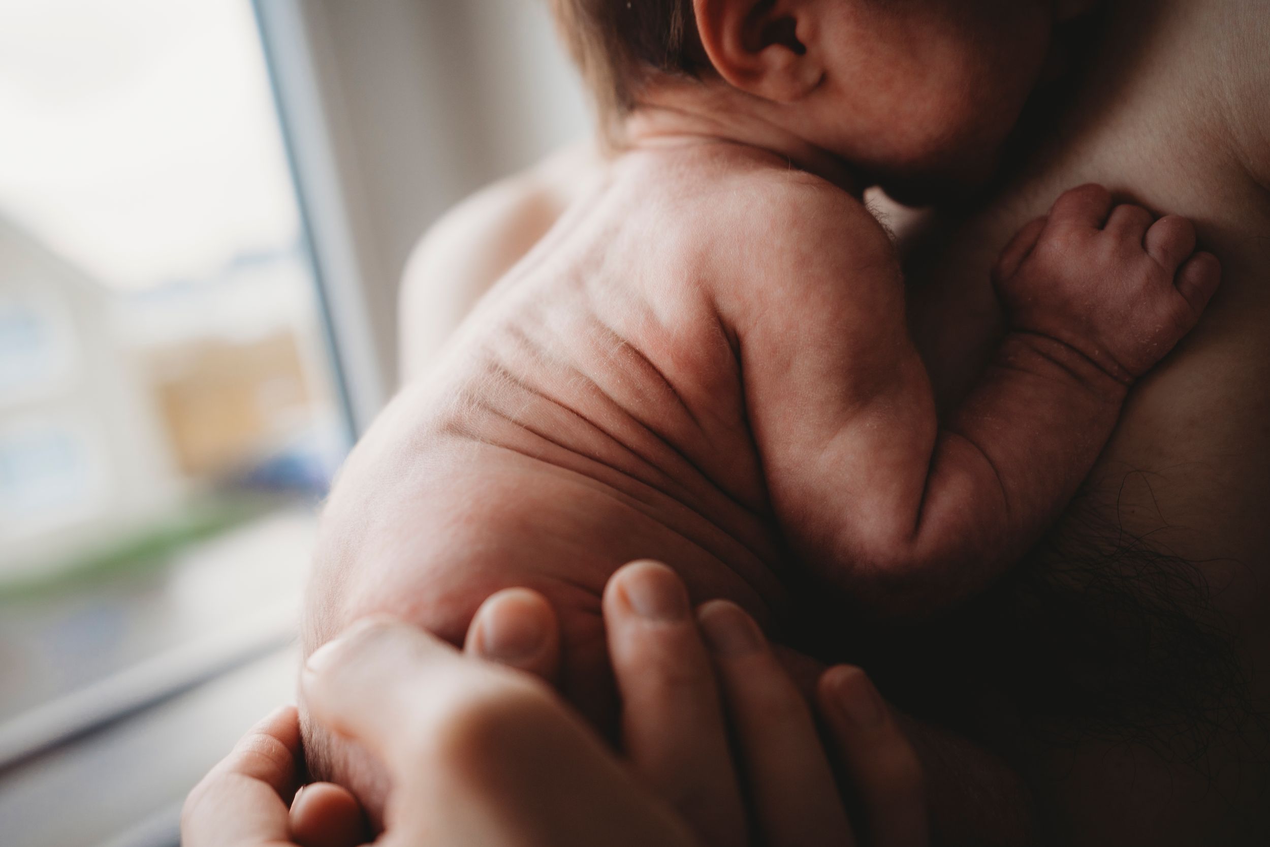 Close-up black and white image of a newborn being held tenderly.