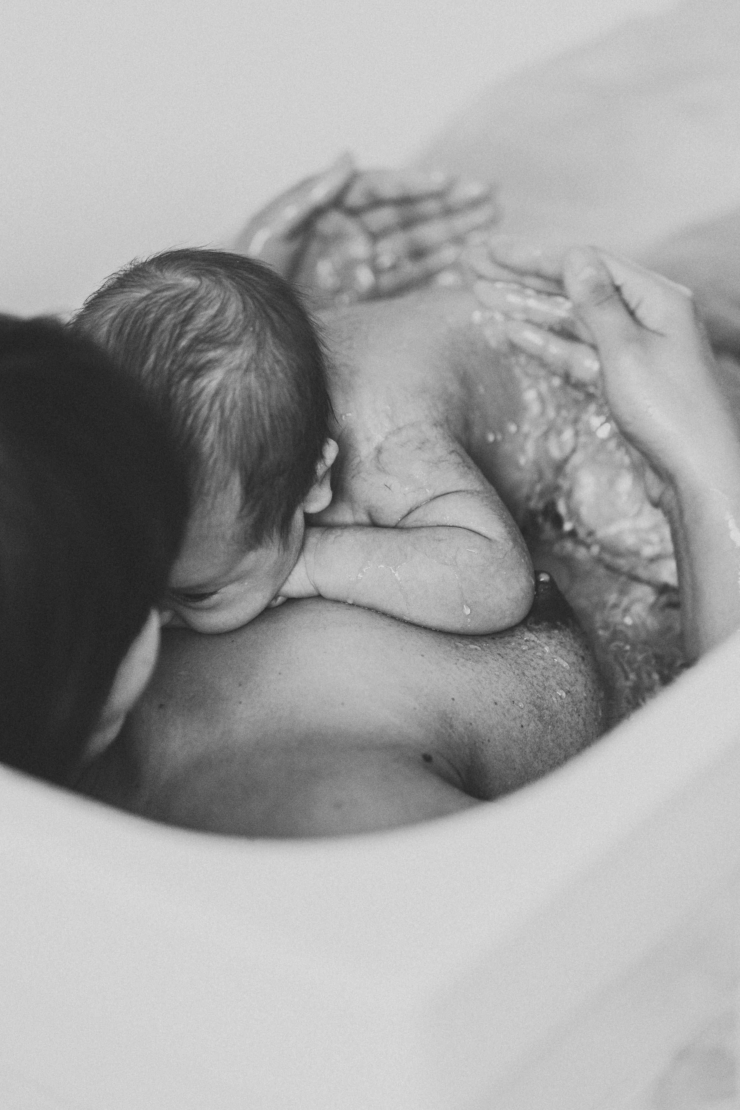 Black and white image capturing a gentle bath time moment with hands supporting a newborn.
