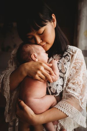 A peaceful moment captured in warm light as a tiny infant is held close in lace-draped arms.