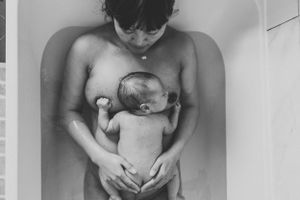 Black and white intimate photograph showing a tender bathing moment with a newborn baby.