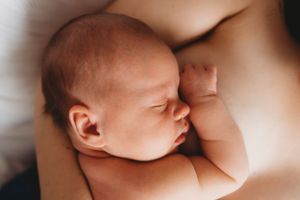 Peaceful sleeping newborn baby resting against soft skin in natural light.