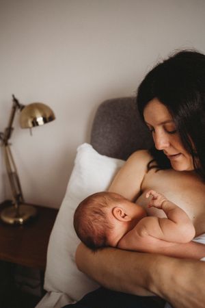 A peaceful intimate moment between a mother nursing her newborn baby next to a desk lamp in a dim room.